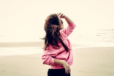 Rear view of woman standing on beach against clear sky