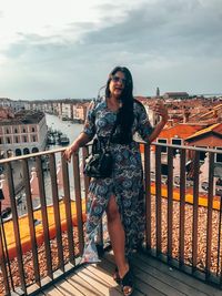 Portrait of smiling woman standing on railing against cityscape