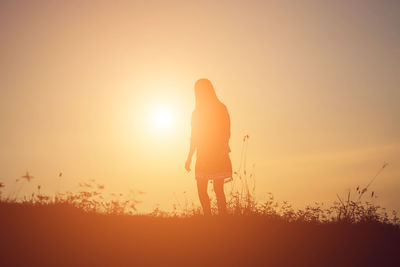 Rear view of silhouette person standing on field against sky during sunset