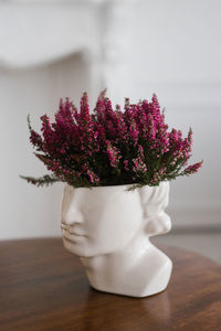 Purple heather at the vase sculpture of the head on the table in the interior of a cozy house