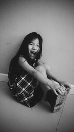 Full length portrait of playful girl screaming while sitting on floor against wall
