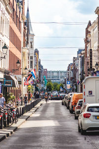 Cars on city street by buildings against sky