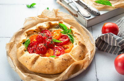 Fresh homemade galette with tomatoes, ricotta cheese and basil on white tile background.