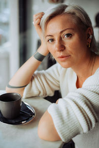 Blond woman sitting at table with cup of coffee looking at camera