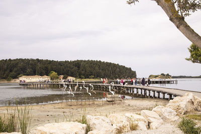 People on bridge over river against sky