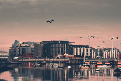 Silhouette city by river against sky during sunset