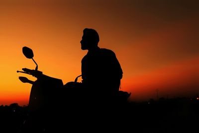 Silhouette man with motorcycle against orange sky during sunset