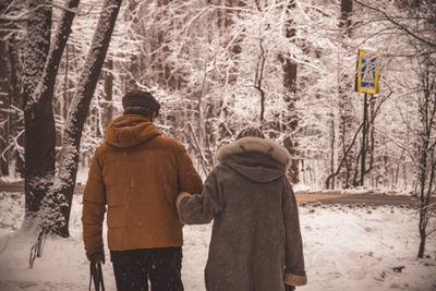 Rear view of couple walking in snow covered forest during winter