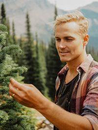 Young man looking at tree while standing in forest