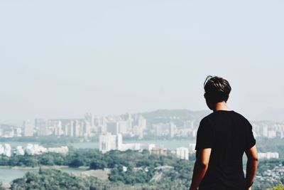 Rear view of man looking at city buildings against clear sky