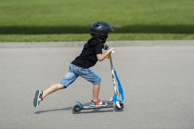 Side view of boy riding push scooter on road