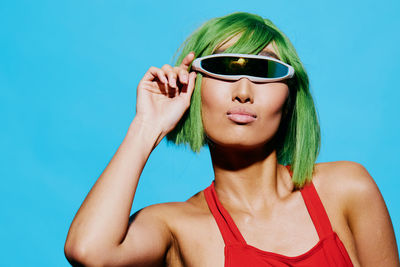 Portrait of young woman wearing sunglasses against blue background