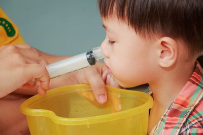 Cropped hand of woman spraying water in boy nose