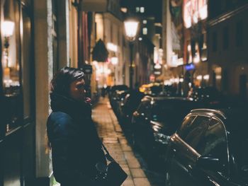 Side view of woman looking at illuminated city at night