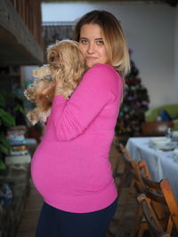 Portrait of pregnant woman holding with dog at home