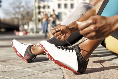 Sportswoman typing shoelace while sitting by man on sidewalk at city