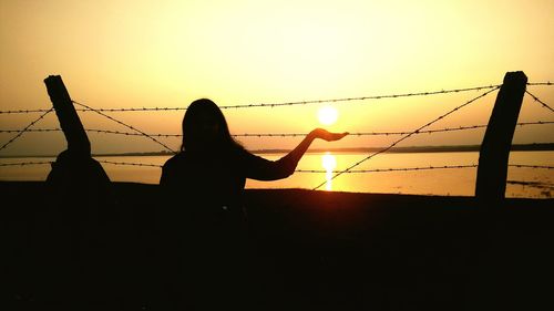 Silhouette man with arms raised against sunset sky