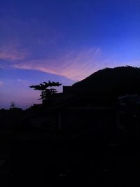 Silhouette house by building against sky during sunset