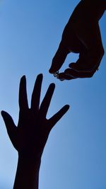 Cropped man putting ring on woman finger against clear sky
