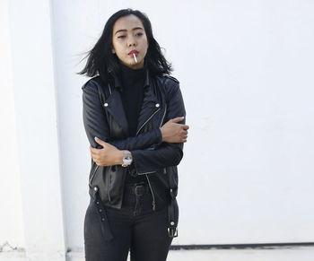 Woman smoking cigarette while standing against wall outdoors