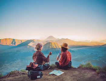 Rear view of people sitting on mountain against clear sky