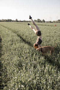 Woman doing handstand by dog on grassy field