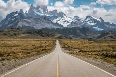 Road leading towards snowcapped mountains against sky