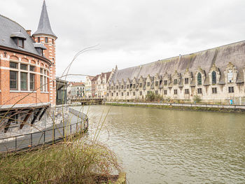 View of buildings by river against sky in city