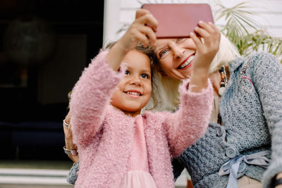 Smiling granddaughter and grandmother taking selfie in mobile phone
