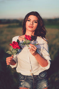 Young woman holding rose while standing on field