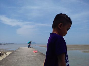 Boy standing on beach against sky