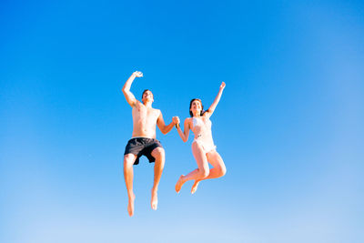 Low angle view of young woman jumping against clear blue sky