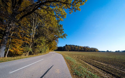 Empty road amidst trees against clear sky during autumn