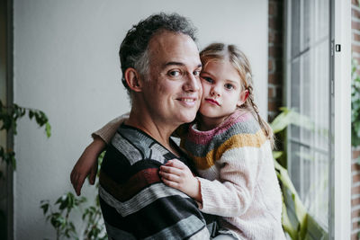 Smiling father carrying daughter while standing by window at home
