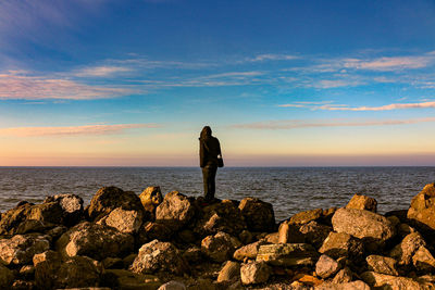 Man standing on rock by sea against sky