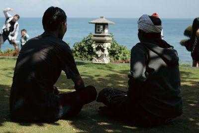 Friends sitting on grass against sea