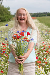 Beautiful middle-aged blonde woman stands among a flowering field of poppies