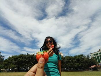 Smiling woman wearing sunglasses holding strawberry against sky
