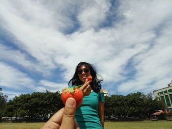 Smiling woman wearing sunglasses holding strawberry against sky