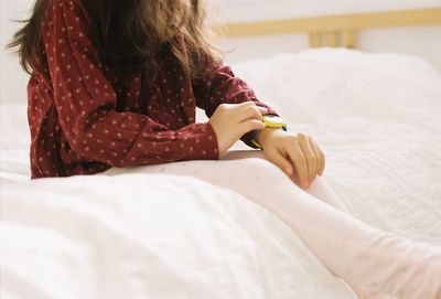 Midsection of girl checking time while sitting on bed at home