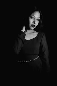 Portrait of young woman standing against black background