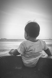 Rear view of boy at beach against sky