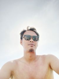 Portrait of shirtless man wearing sunglasses against sky