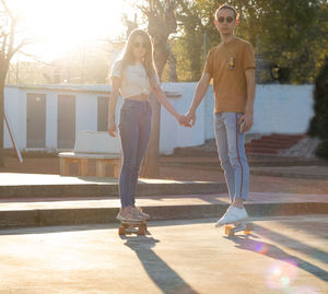 Gorgeous young couple skating together on their cruiser boards while holding hands at sunset