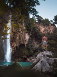 Man standing on rock against waterfall