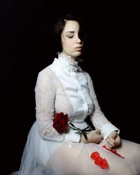 Unhappy bride with rose flower sitting against black background