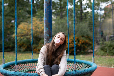 Portrait of smiling young woman sitting on swing at playground