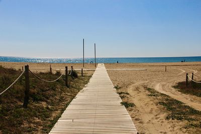 Boardwalk leading towards beach against clear sky