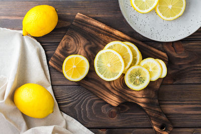 Sliced round pieces of lemon on a cutting board and whole lemons on a wooden table. 