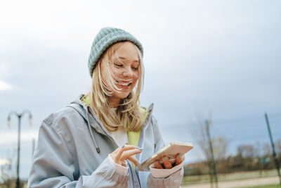 Smiling blond girl using mobile phone under sky